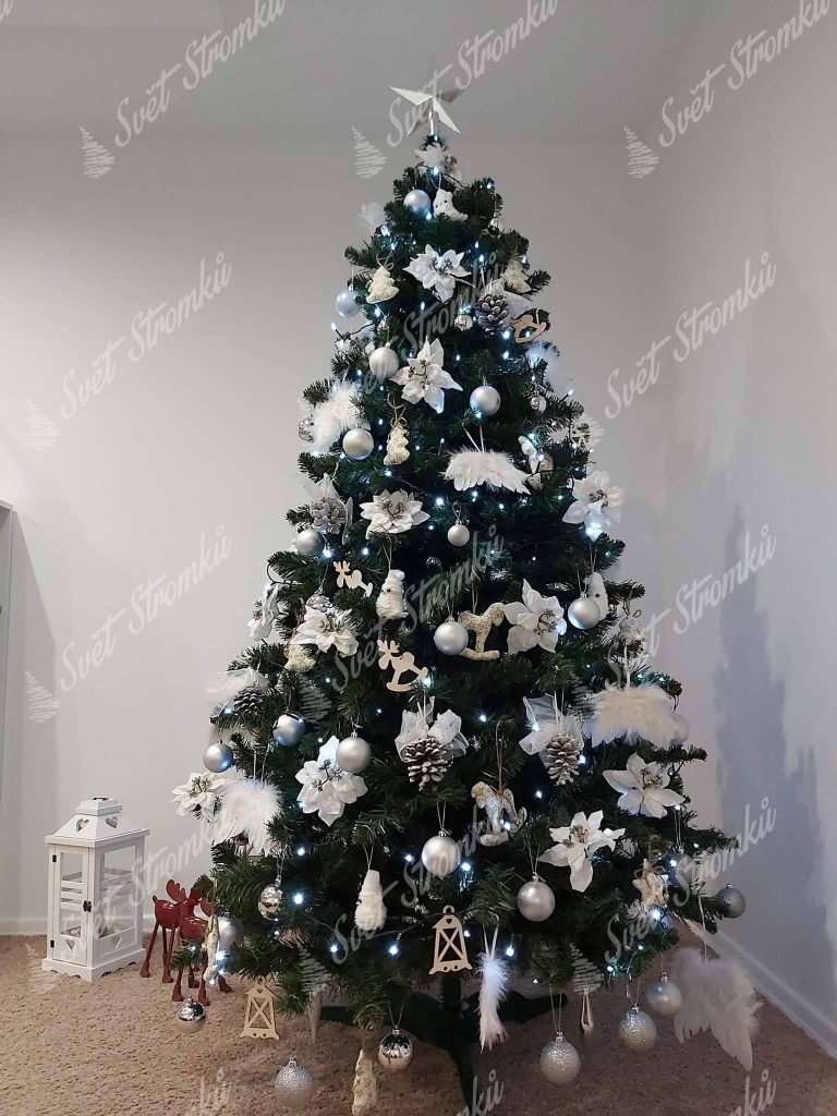 Zelený vánoční stromek ozdobený bílými květy, šiškami a andělskými křídly.